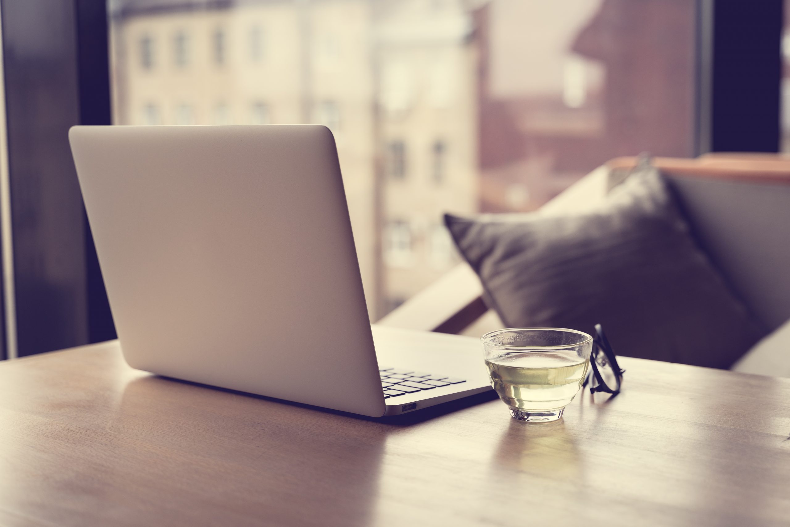 Freelance Desk with open laptop, cup of green tea and glasses on table. Cafe or coworking space. Concept of digital nomads, home office, blogging. No people.